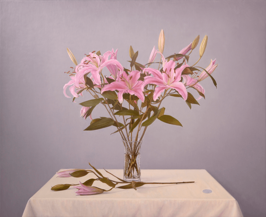 A realist still life oil painting on panel titled 'Lilies,' measuring 20 inches by 24 1/4 inches. A lush arrangement of pink lilies with prominent orange stamens is held in a clear glass vase filled with water. The vase sits on a cream coloured tablecloth, a silver coin rests near the right corner, as a single flowered stem lays across the small table in front of the vase. Soft, directional light from the left creates bright, crisp highlights on the waxy petals and the crystal glass, while the coin's surface reflects on it's own. The background is a neutral, toned grey. Oil painting by John Hansen.