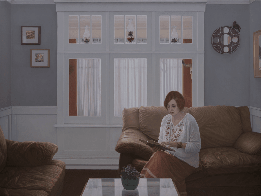 A realist figurative oil painting on panel titled 'Woman Reading,' measuring 30 inches by 40 inches. A woman with short, dark hair is shown backlit, seated and deeply absorbed in a book held open in her hands. She wears a embroidery detailed white blouse and a suede skirt, and her figure is illuminated by a warm, soft light from the left. The background is a dark, atmospheric interior with framed paintings and an art-crafted mirror hanging on the wall behind her. The lighting highlights the texture of the book pages and the gentle contour of her features. Oil painting by John Hansen.